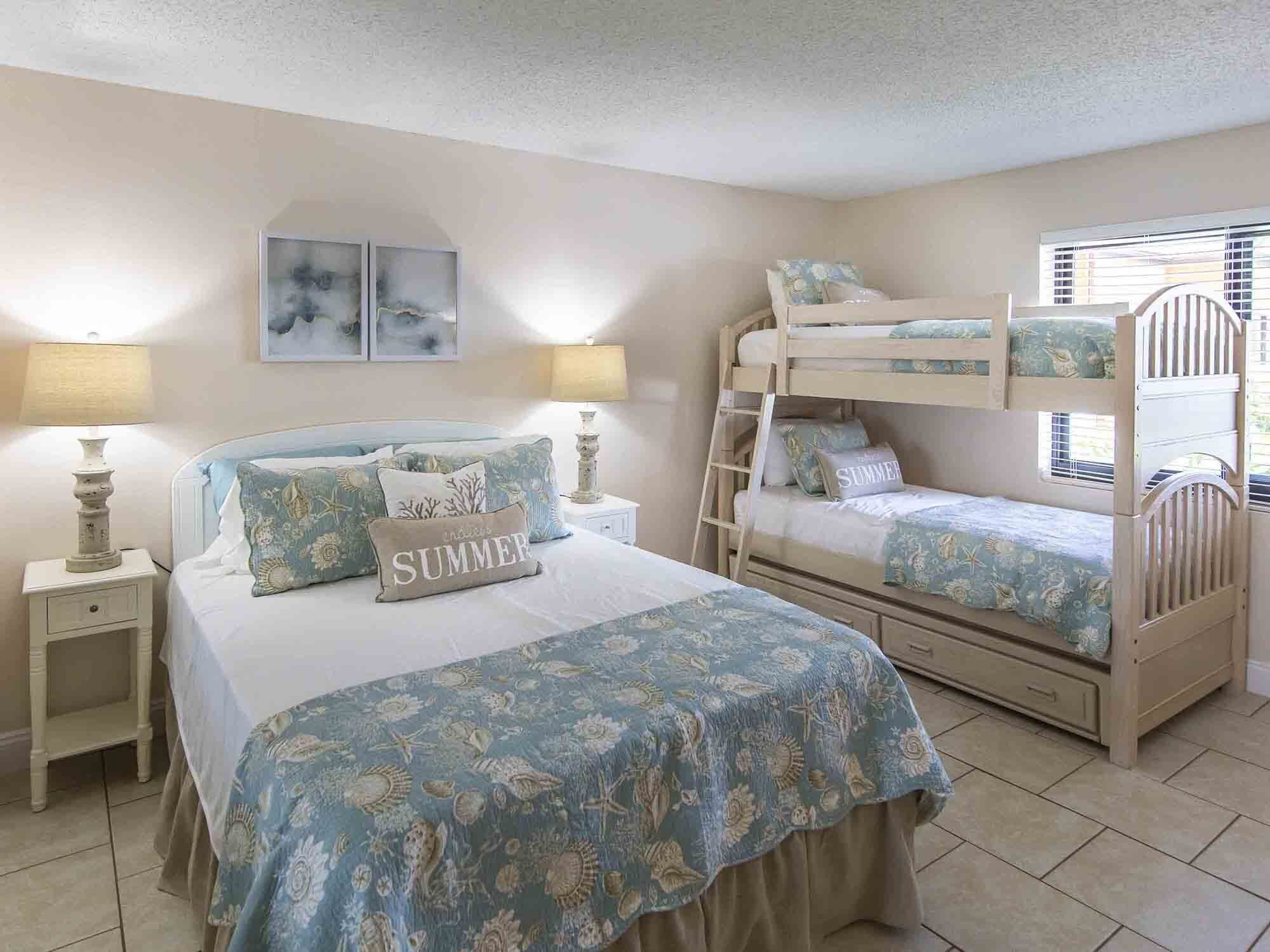 Un dormitorio con una cama litera, una cama individual y una mesita de noche con lámparas.