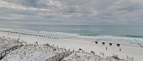 A beach with a wooden boardwalk leading to the shore, a sandy beach, and a cloudy sky.