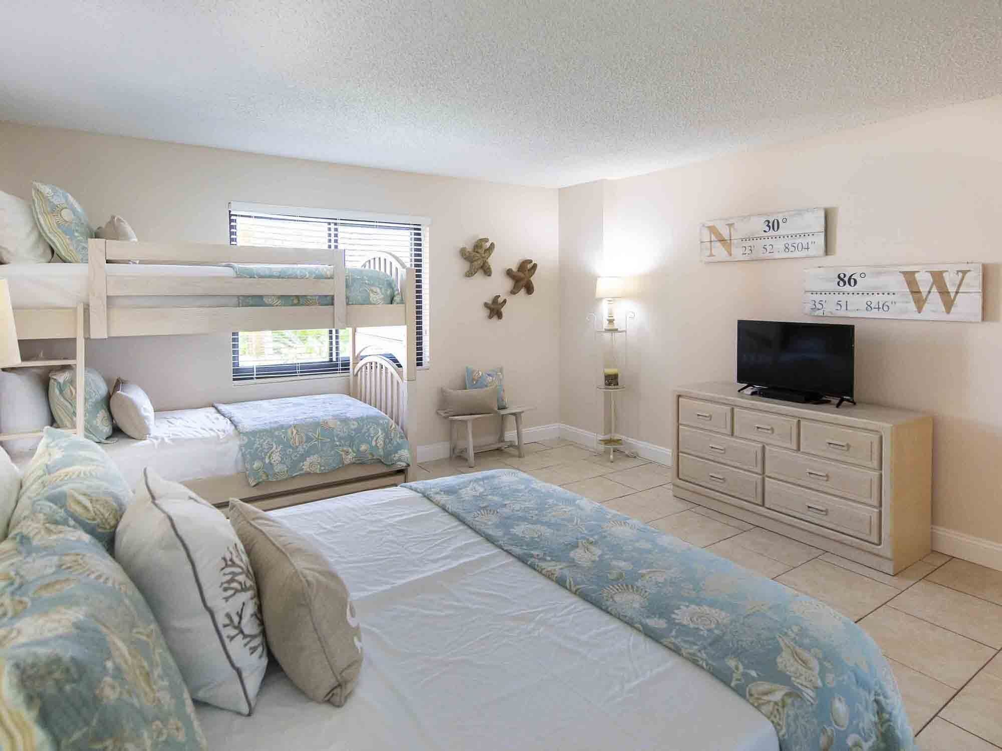 Un dormitorio con literas, televisión, cómoda y decoración en la pared.