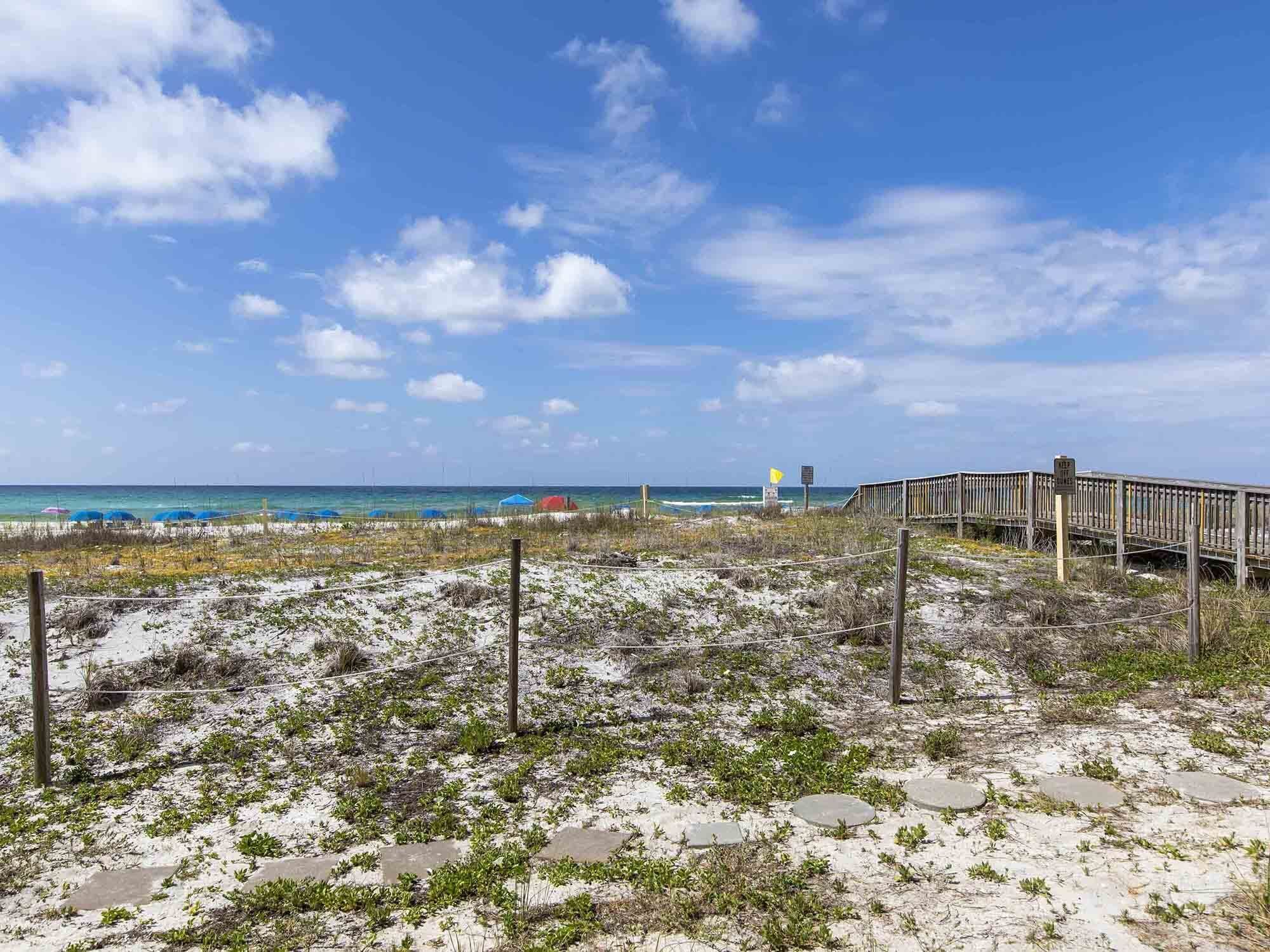 A beach with a wooden boardwalk, a sandy path with stepping stones, and a clear view of the ocean.