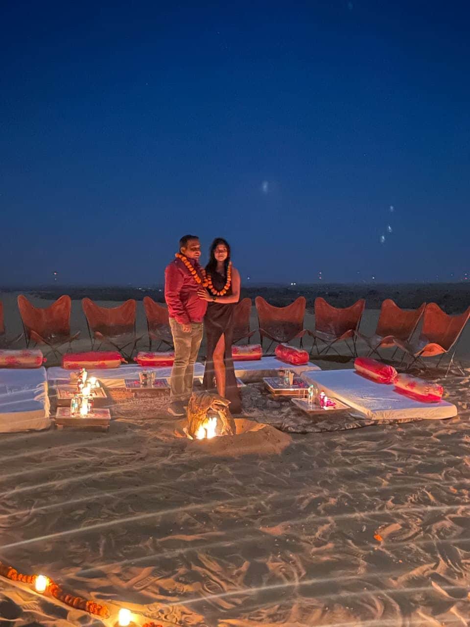 A couple standing on a beach with chairs and tables arranged for an outdoor event.