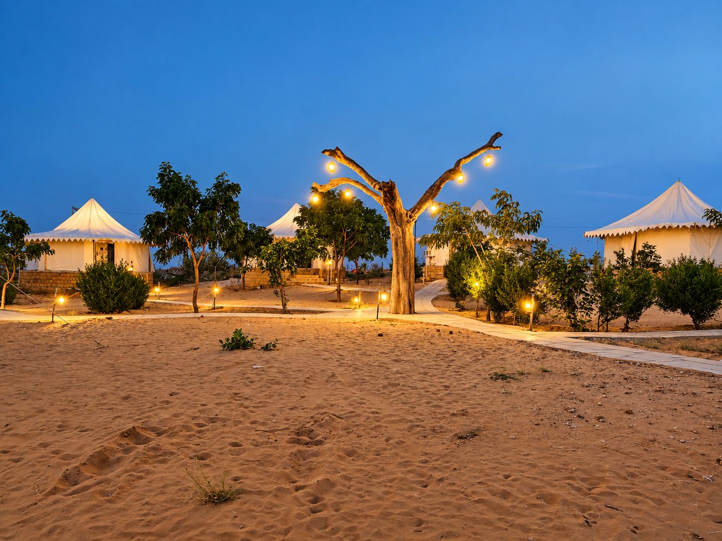 A desert landscape with multiple yurts and a central tree adorned with lights.