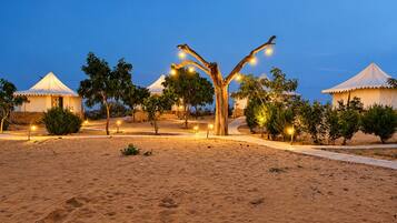 A desert landscape with multiple yurts and a central tree adorned with lights.
