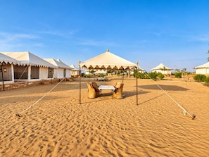 Ein Camp in der Wüste mit Zelten und einem Tisch mit Stühlen.