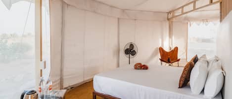 Habitación con carpa, una cama, una silla, un ventilador y una bandeja con tetera y botellas.