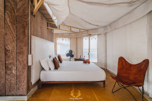 A spacious tented room with a large bed, a wooden floor, and a fan.