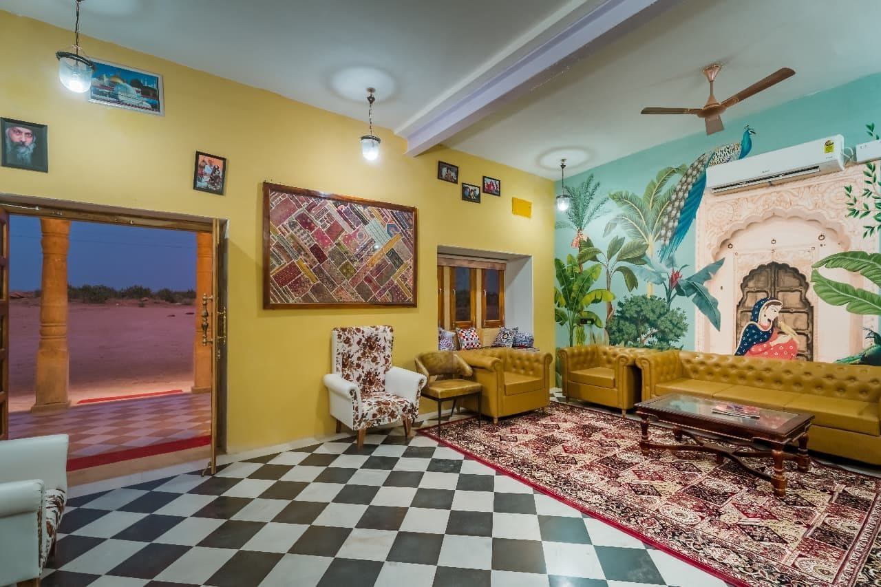 A living room with a checkered floor, a sofa set, a patterned rug, and a mural on the wall.