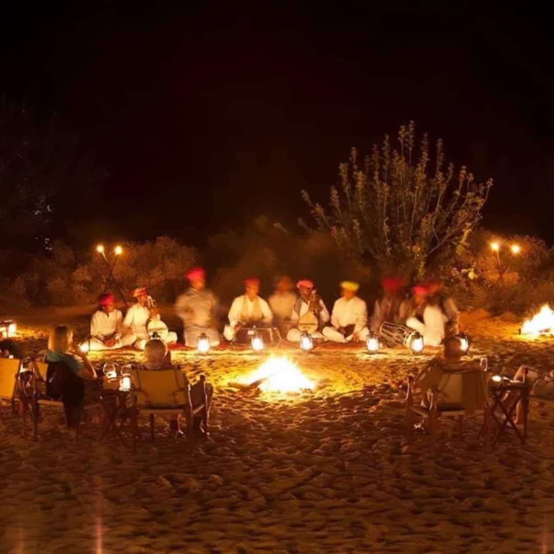 Eine Gruppe von Menschen sitzt an einem Lagerfeuer in einer Freiluftumgebung.