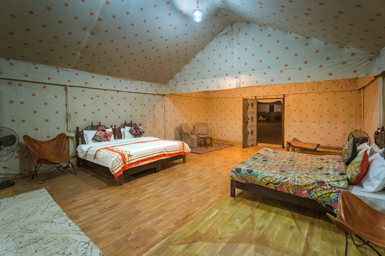 Una habitación con dos camas, una silla, una mesita y una puerta que da a otra habitación.