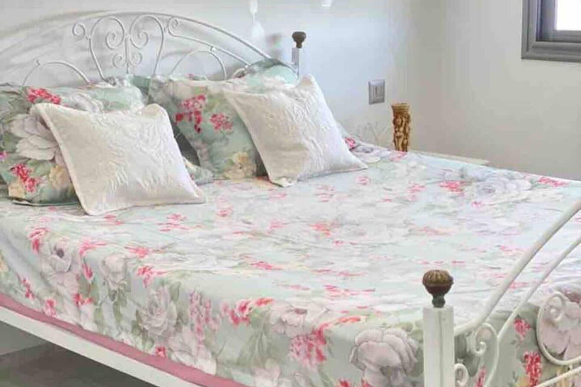 Una cama con colcha estampada, almohadas blancas, cabecero de metal y una mesita de noche con lámpara.