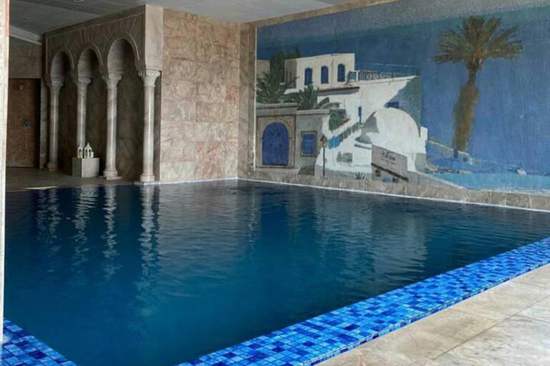 A swimming pool with a tiled edge, a mural of a building, and columns.
