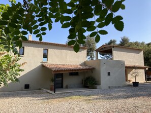 Une maison à deux étages, avec un toit en tuiles, une terrasse couverte et une allée gravillonnée.