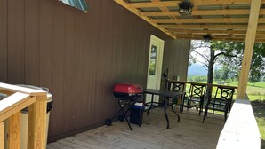 Un patio techado al aire libre con una mesa y sillas de madera, una parrilla y un bote de basura.