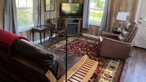 Una sala de estar con un sofá de cuero, una mesa de centro de madera, un televisor, una chimenea y un ventanal con cortinas.