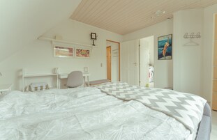Un dormitorio con cama, escritorio y silla. Una puerta da a otra habitación.