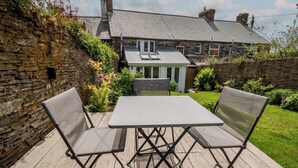 Een terras met een tafel en stoelen, een stenen muur en een huis op de achtergrond.