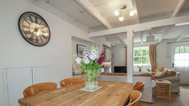Een eethoek met een houten tafel, stoelen, een klok en een vaas met bloemen.