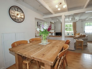 A dining area with a wooden table, chairs, a clock, and a vase with flowers.