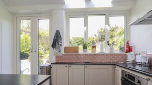 Een keuken met een tegelwand, witte kastjes, een zwart aanrechtblad en een raam met uitzicht op groen.