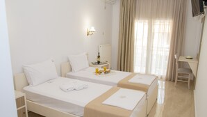 Ein Hotelzimmer mit zwei Betten, einem kleinen Tisch mit Flasche und Gläsern, einem Sessel und einem an der Wand befestigten Fernseher.