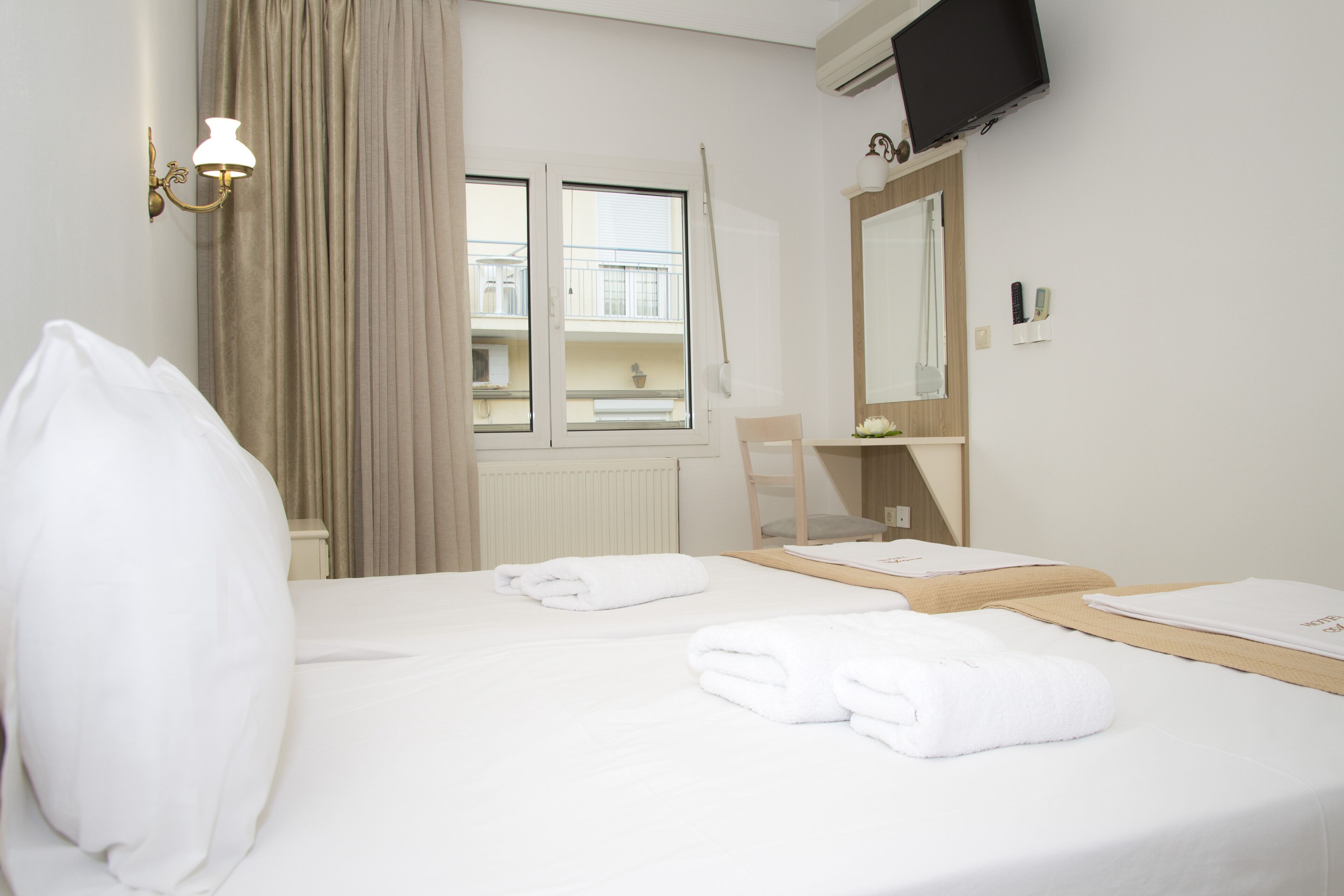 A hotel room with a bed, a window with curtains, a television mounted on the wall, and a mirror.