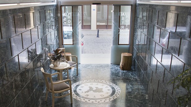 Eine Lobby mit Marmorboden, einem Holzstuhl, einem kleinen runden Tisch und einem Hocker.
