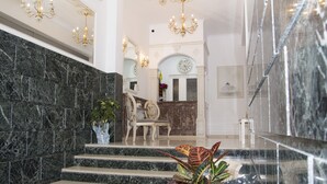 Eine Marmortreppe führt zu einem Empfangsbereich mit einer Uhr, einem Chandelier und einem Sessel.