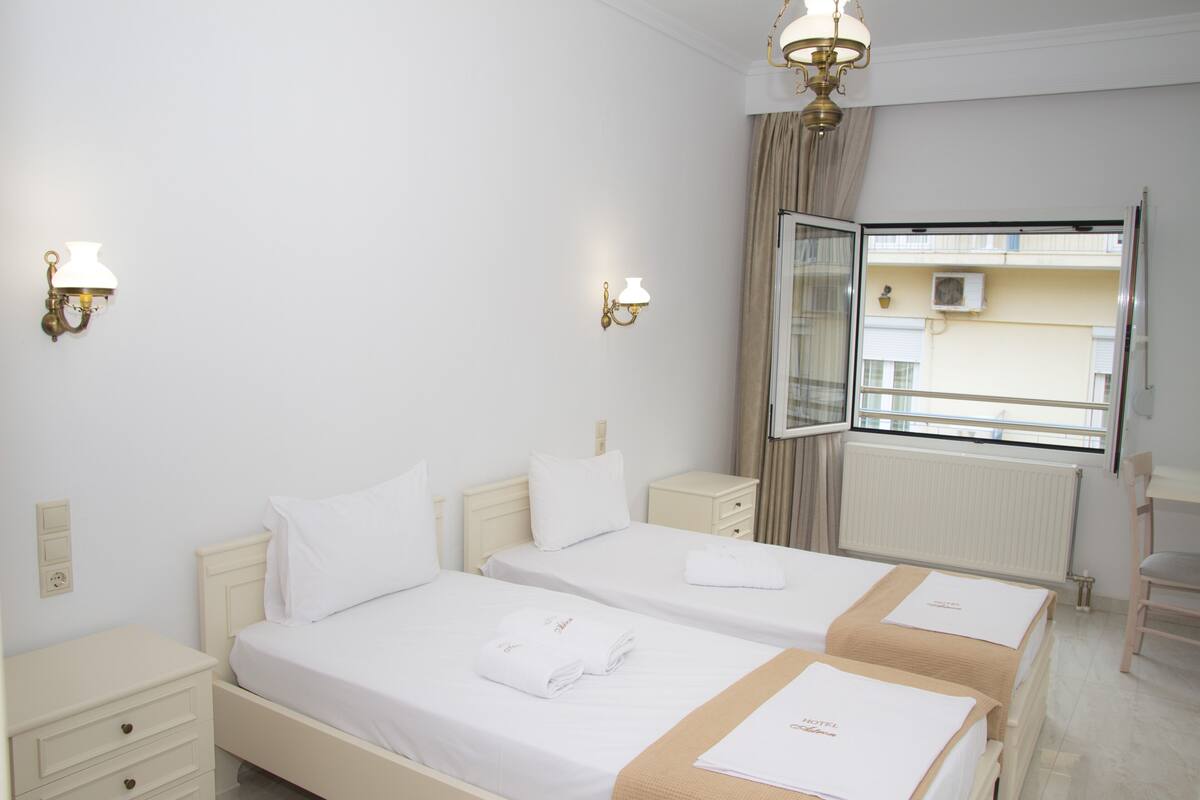 Habitación de hotel con dos camas, una mesita de noche, un aparador y una ventana con vistas al exterior.