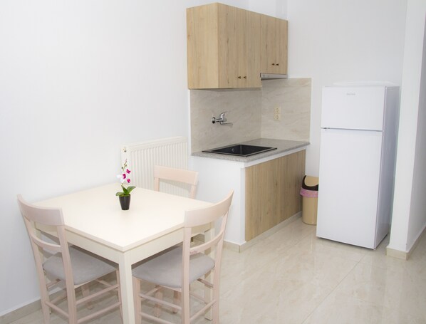 Una cocina pequeña con una mesa blanca, sillas, un lavamanos y un refrigerador.