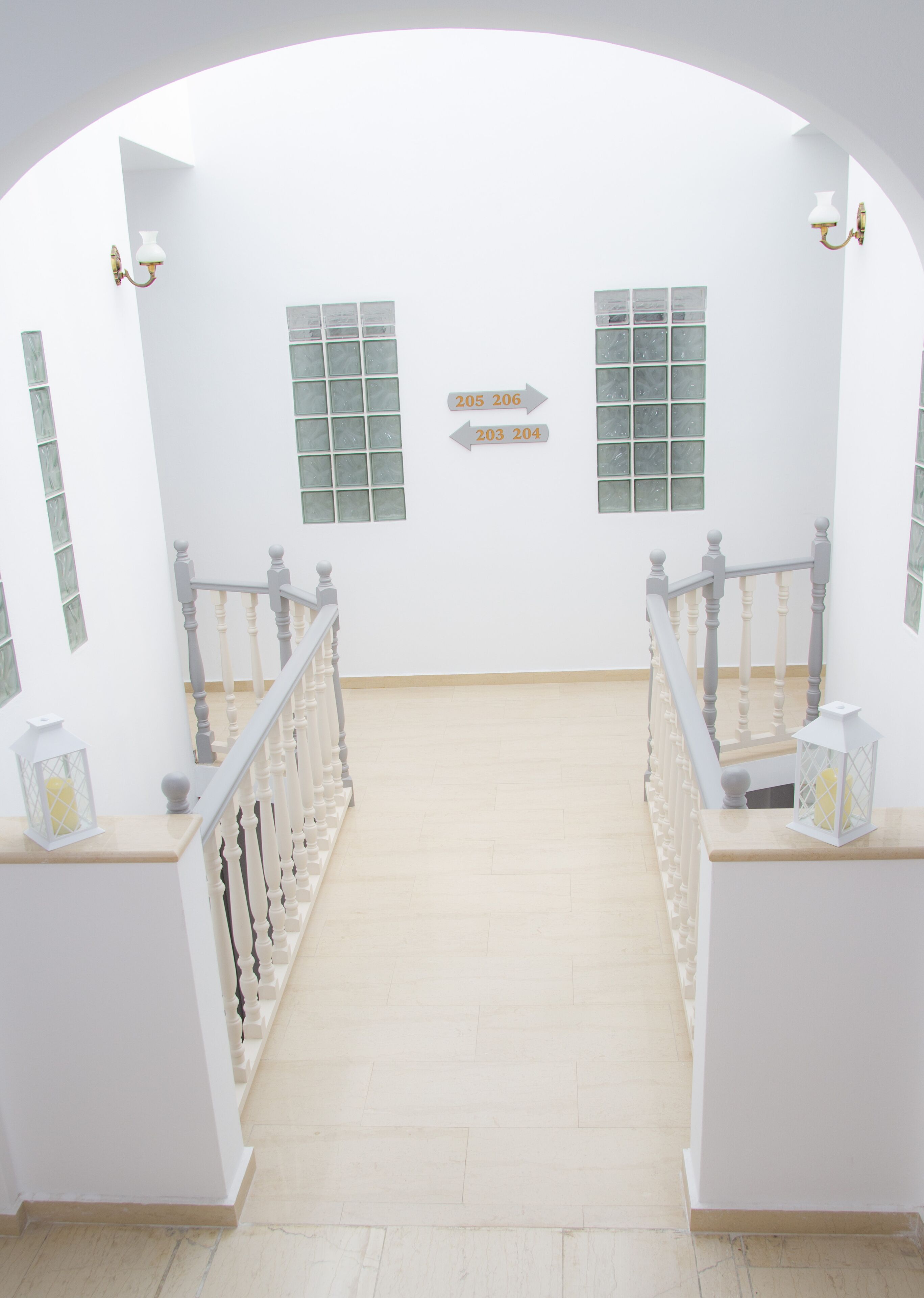 A staircase with white railings and a light-colored floor, leading to a room with two windows and a wall-mounted sign indicating room numbers.