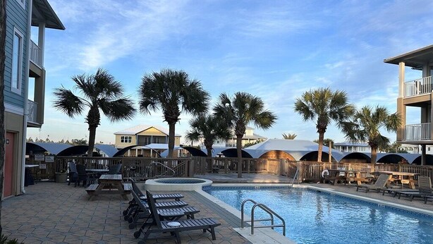 A pool area with lounge chairs, palm trees, and covered seating areas. - Canal Front Condo "Shore Thang" (Mexico Beach)