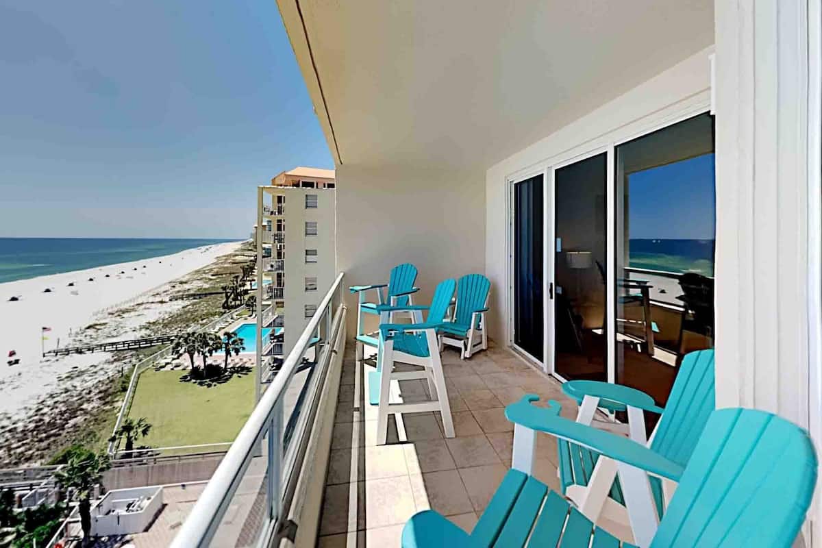 A balcony with turquoise chairs overlooking a beach.