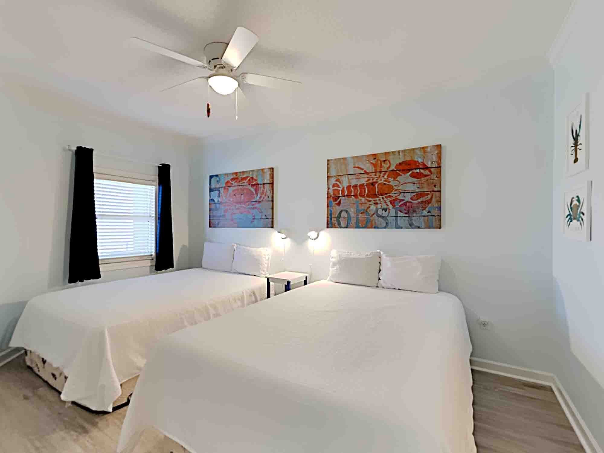 Habitación de hotel con dos camas, ventilador de techo y obras de arte en las paredes.