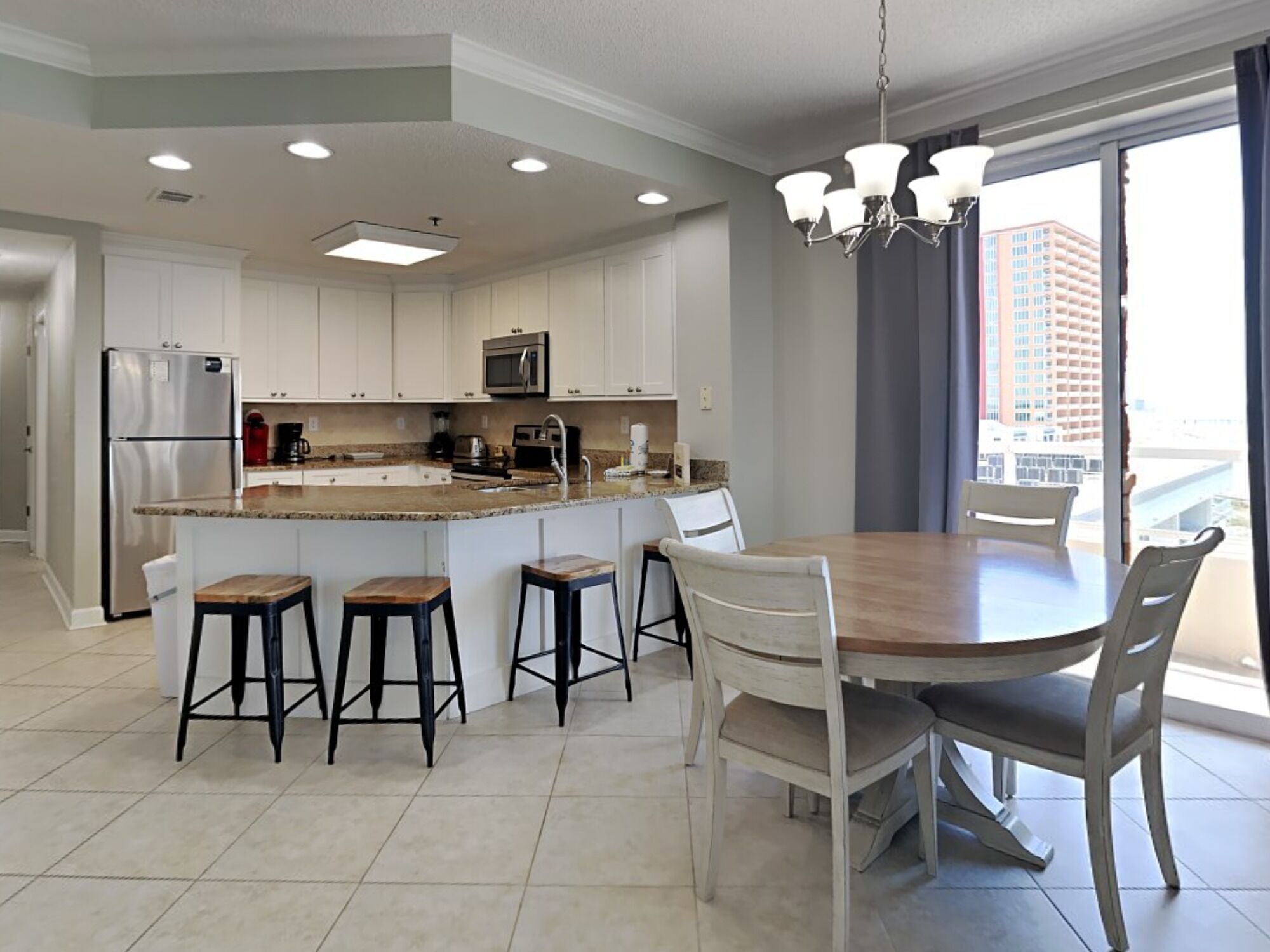 A modern kitchen with a central island, bar stools, a dining table, and a chandelier.