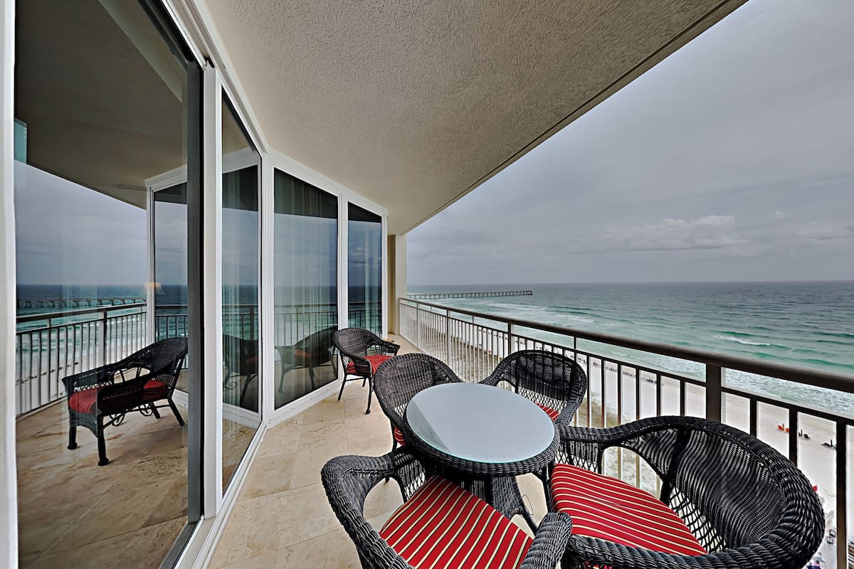 A balcony with wicker furniture and a glass door leading to the ocean.