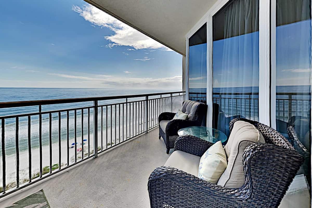 A balcony with a view of the ocean, furnished with wicker chairs and a glass table.