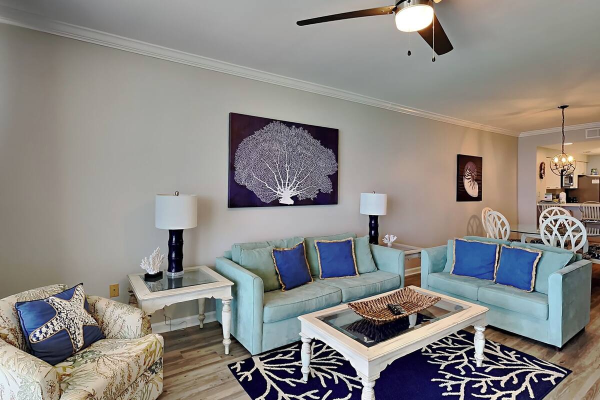 A living room with two light blue sofas, a glass coffee table, and a ceiling fan.