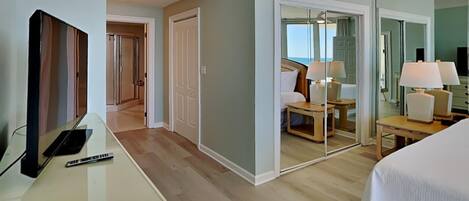 A hotel room with a bed, a desk with a laptop, a TV, and a mirror reflecting the room.