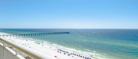 A beach with a pier extending into the ocean, a white sandy beach, and a clear blue sky.