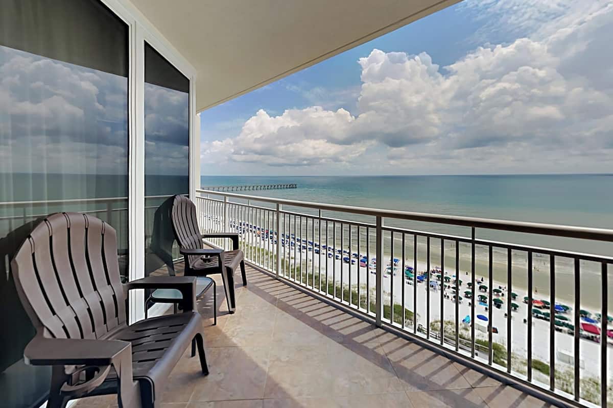 A balcony with two chairs, a view of the beach, and a clear sky.
