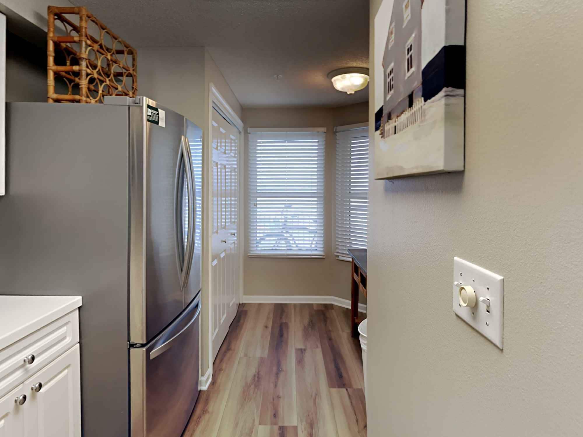 A kitchen with a stainless steel refrigerator, wooden flooring, and white cabinetry.