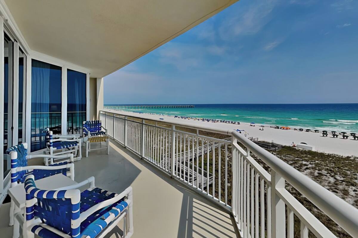A balcony with a view of a beach, a pier, and a clear sky.