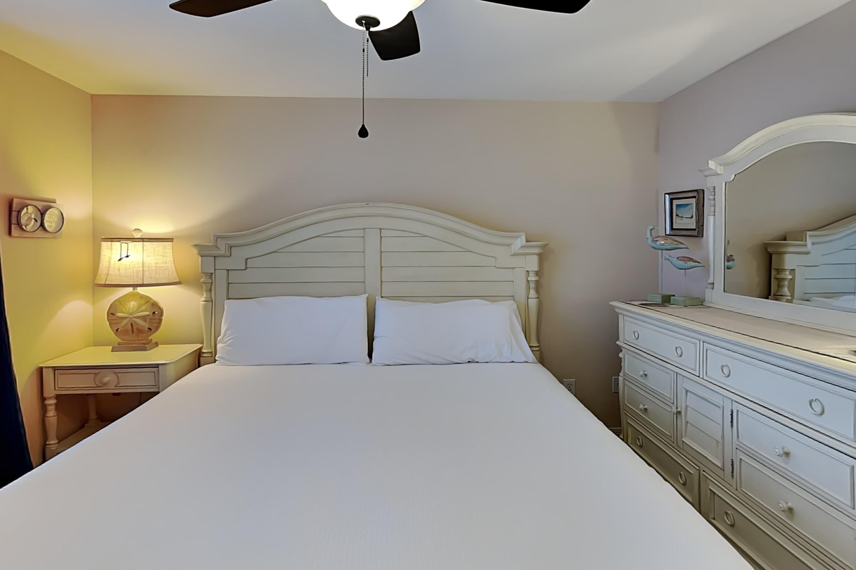 Un lit bien fait, avec du linge de lit blanc, une lampe de chevet, une horloge et une commode à tiroirs.