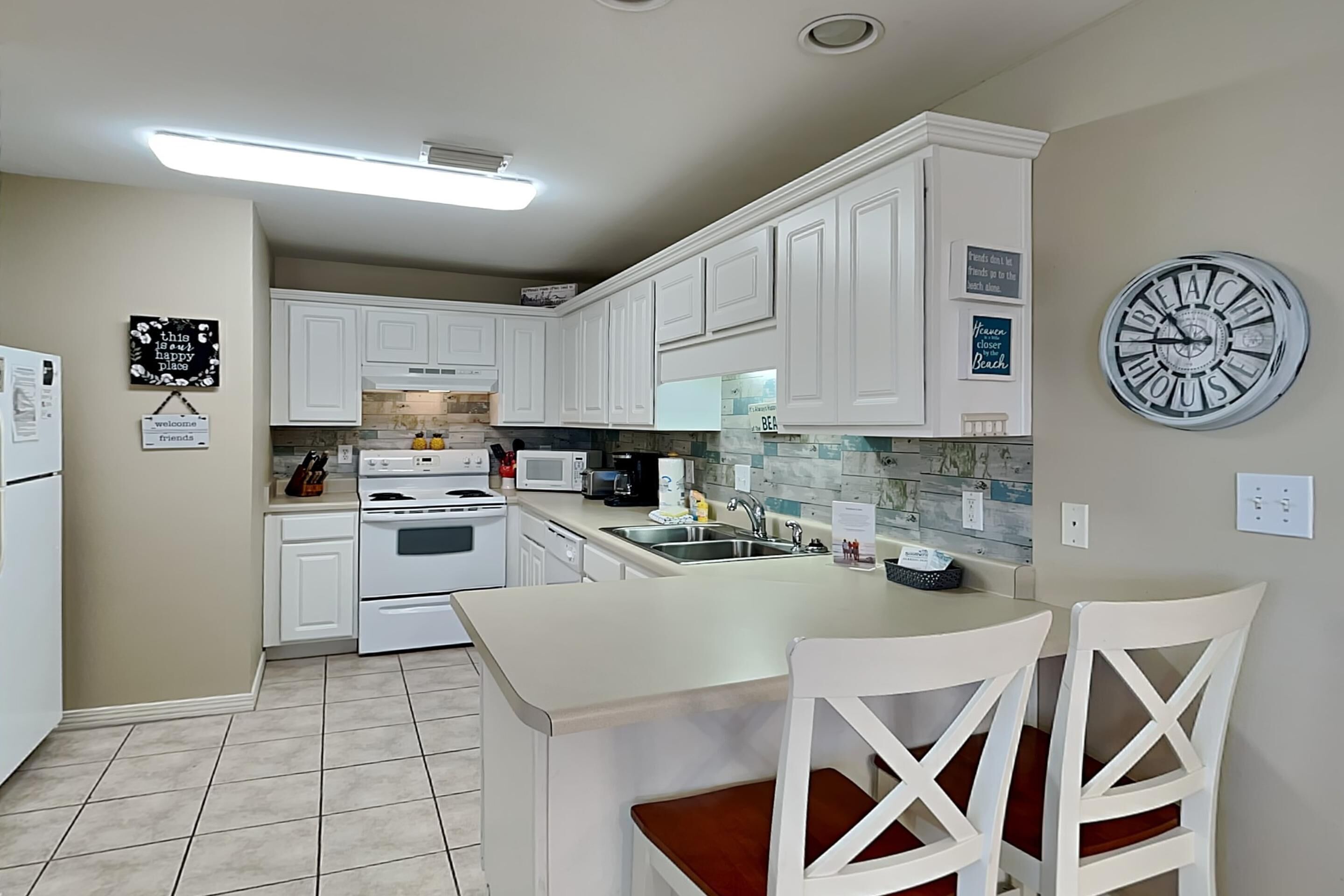A kitchen with white cabinets, a central island with chairs, a clock, and various appliances.