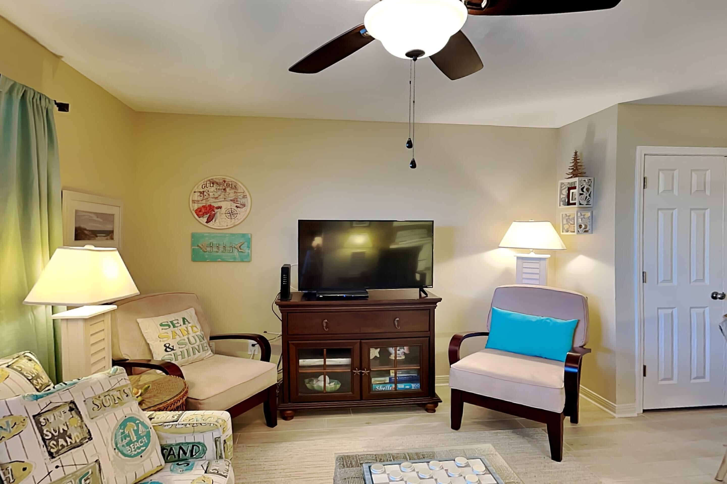 A living room with a ceiling fan, a television, a cabinet with glass doors, and two chairs.