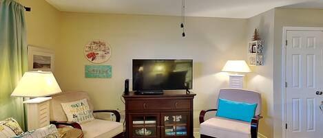 A living room with a ceiling fan, a television, a cabinet with glass doors, and two chairs.