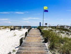 A wooden boardwalk leading to a beach with sand dunes and a flag on a pole. - Three C's by Southern Vacation Rentals (Gulf Shores)