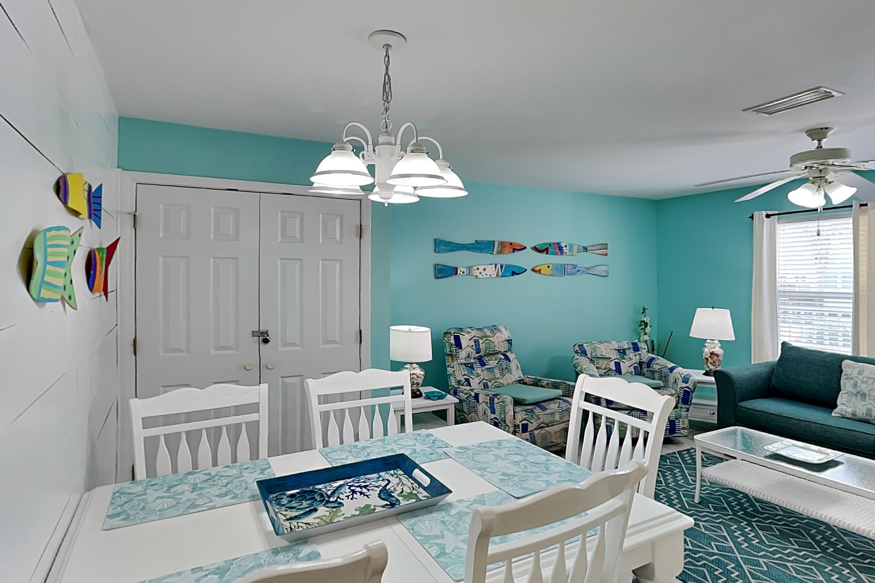 A room with teal walls, a dining table with white chairs, a sofa, and a ceiling fan.