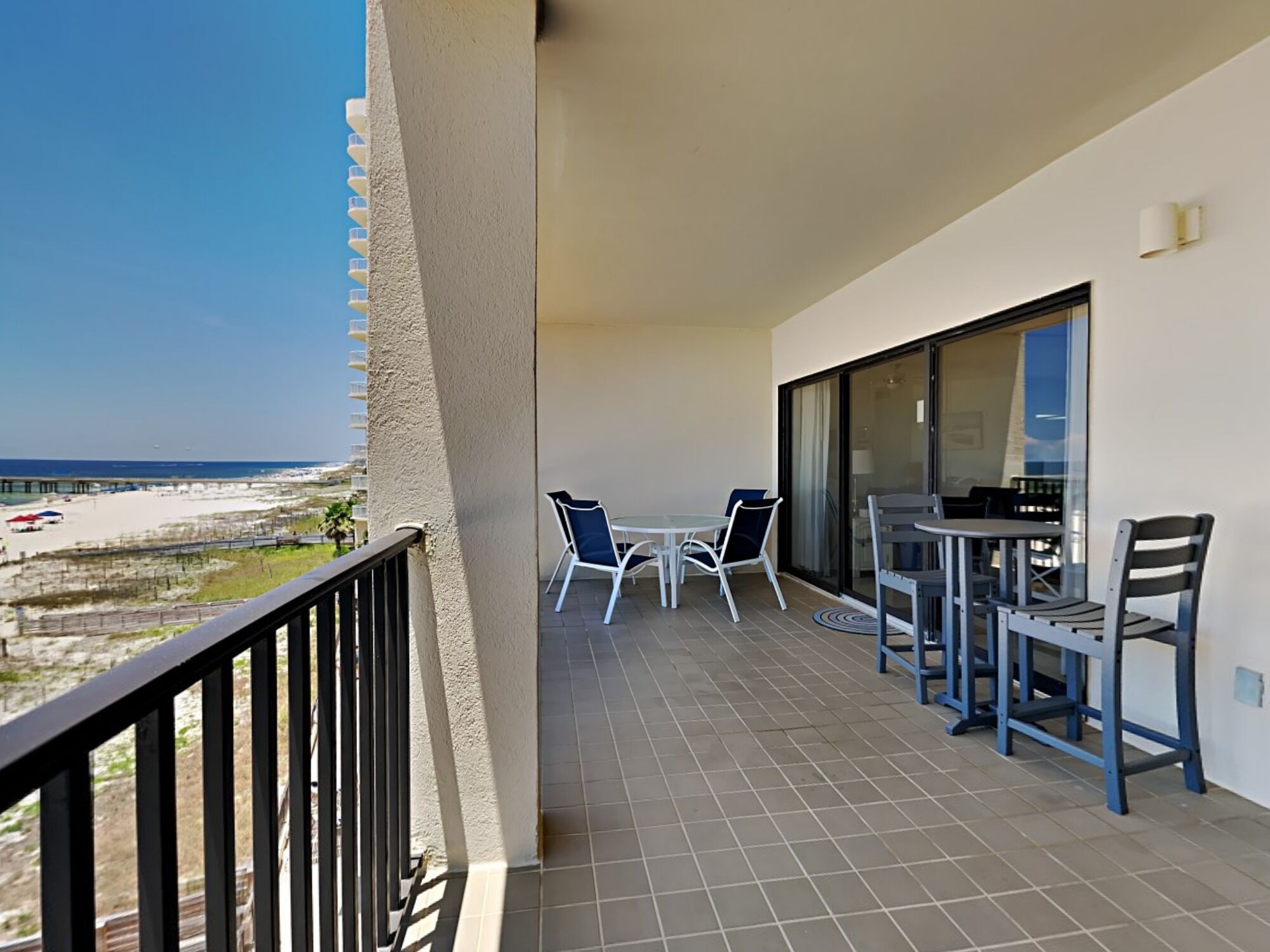 A balcony with a view of the beach, a table with chairs, and a large window.