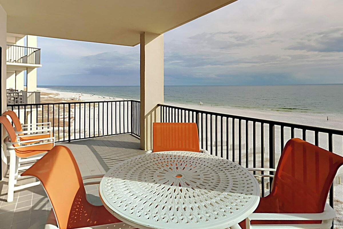 A balcony with a round table and chairs, overlooking a beach.